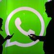 Dos personas hacen uso de sus teléfonos móviles, ante el logotipo de WhatsApp.