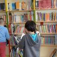 Tres alumnos de primaria consultan libros en una biblioteca escolar.