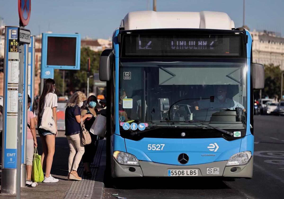 Varias personas, con mascarilla, hacen cola para subir a un autobús de la Empresa Municipal de Transportes madrileña (EMT)