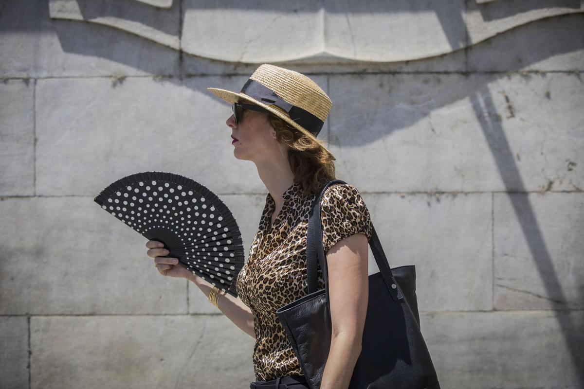 Una mujer se abanica mientras camina por una calle de Sevilla.