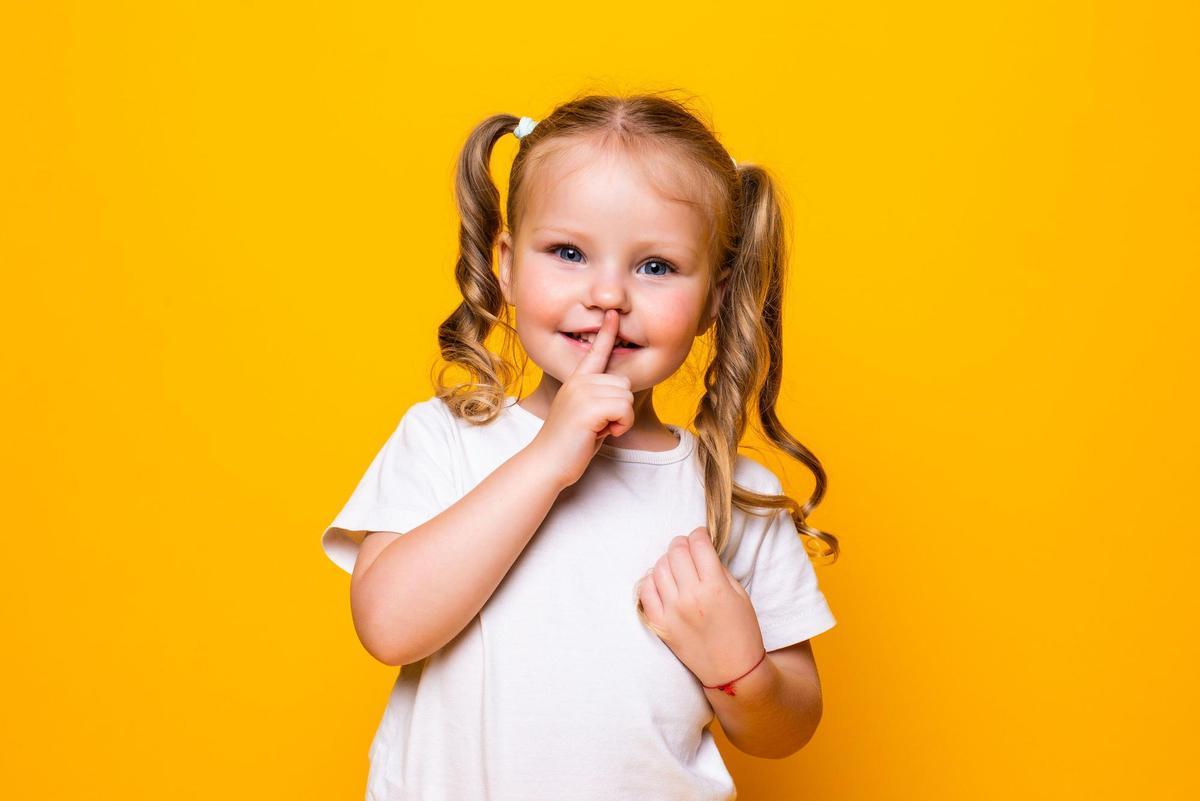 Little girl with her finger over mouth saying Shh isolated over yellow background