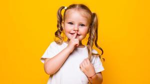 Little girl with her finger over mouth saying Shh isolated over yellow background